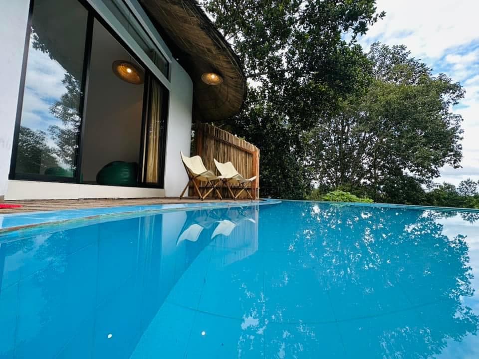 Ground-level view of the pool deck beside the thatched-roof room, with two lounge chairs and the open room doorway visible
