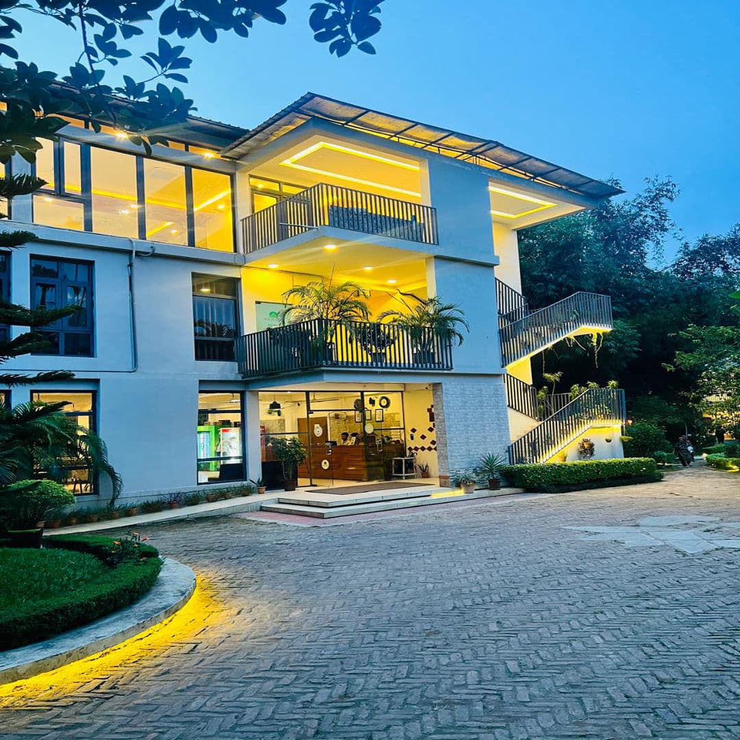 Balishira Resort's three-storey building lit up at dusk, with a staircase and balconies overlooking the entrance drive