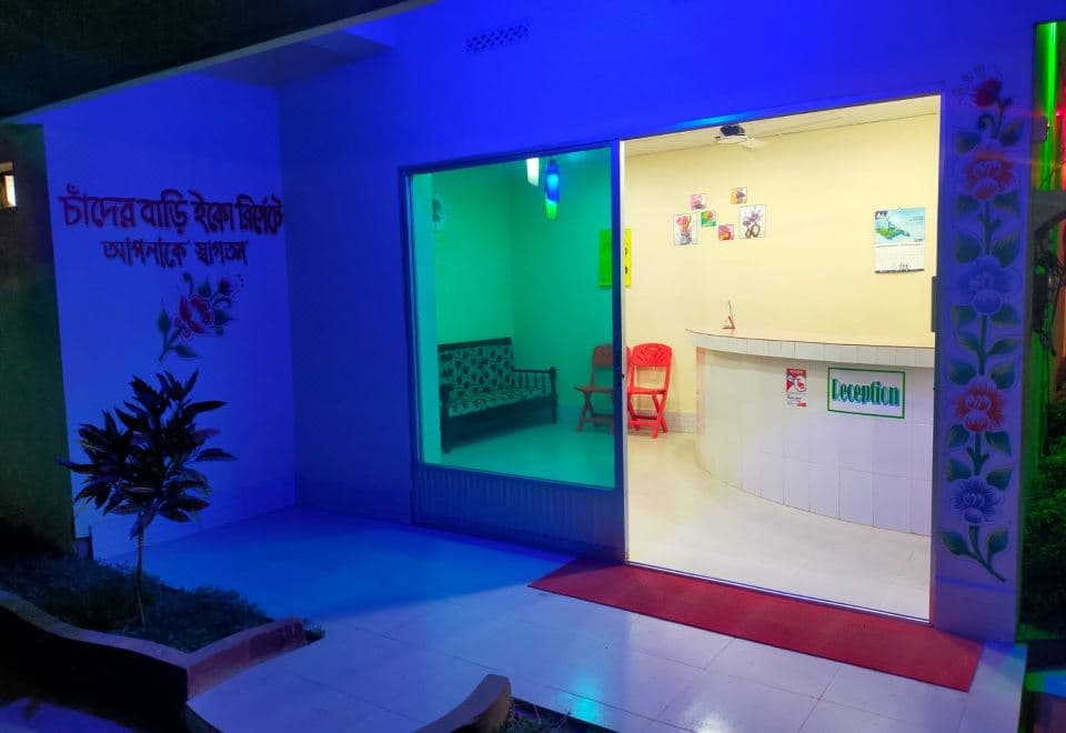 Chader Bari Eco Resort's reception at night, with the resort's name hand-painted in Bangla on the entrance wall