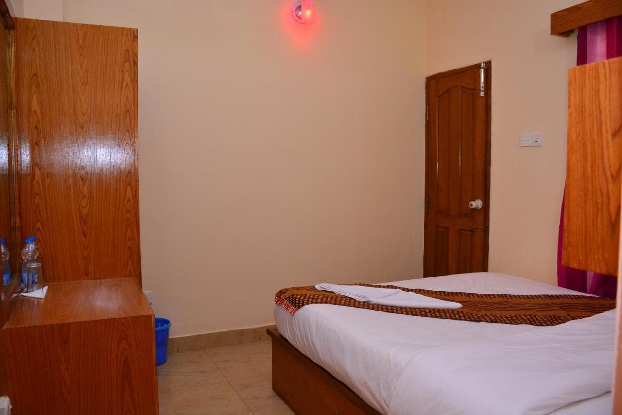 Hotel room interior showing a wardrobe, wall-mounted alarm light, and a bed with a folded runner, wooden door leading to an ensuite