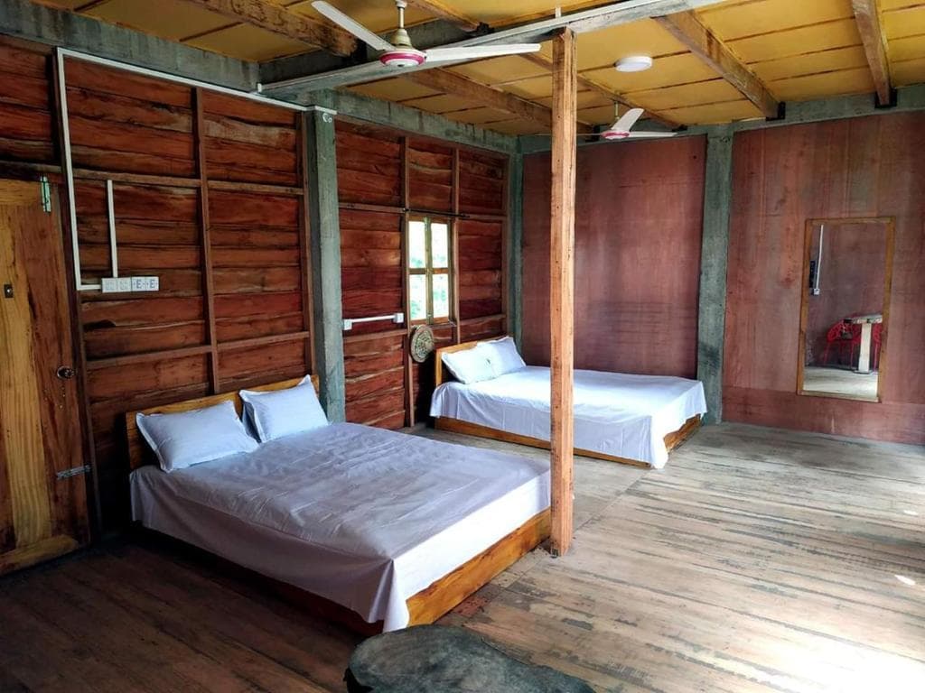 A raw-timber room at Jungle Cottage with two beds, exposed wooden posts, and a ceiling fan