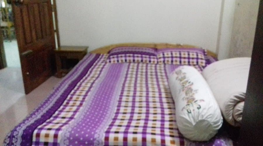 A double bed with a purple checked bedspread and matching pillows in a guest room