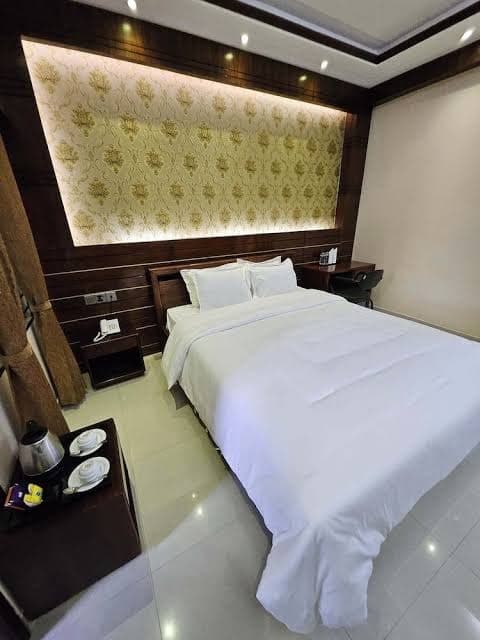 Guest room with a dark wood-paneled headboard framing gold floral wallpaper, white bedding, and a bedside coffee/tea tray with kettle