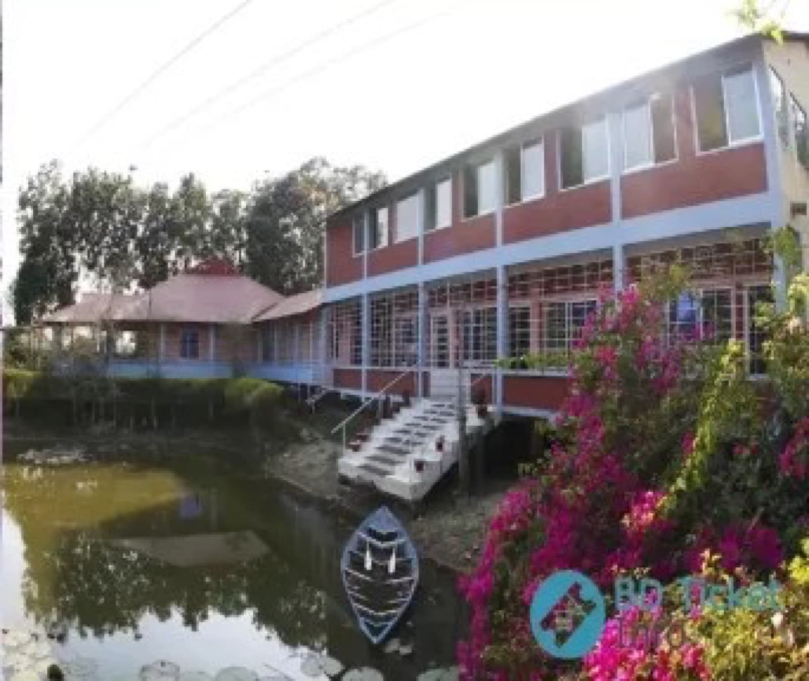 Sreemangal Resort's building beside a pond, framed by flowering bushes