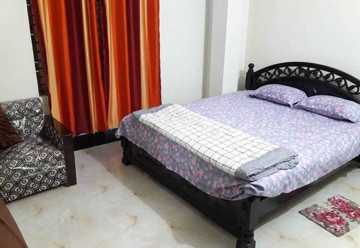 A guest room with a black wrought-iron double bed, floral bedding, and orange curtains