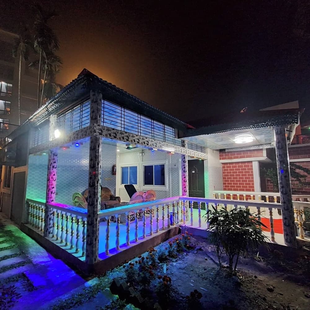 Night view of the veranda with colourful LED accent lighting, wicker chairs, and a brick and white-tile facade